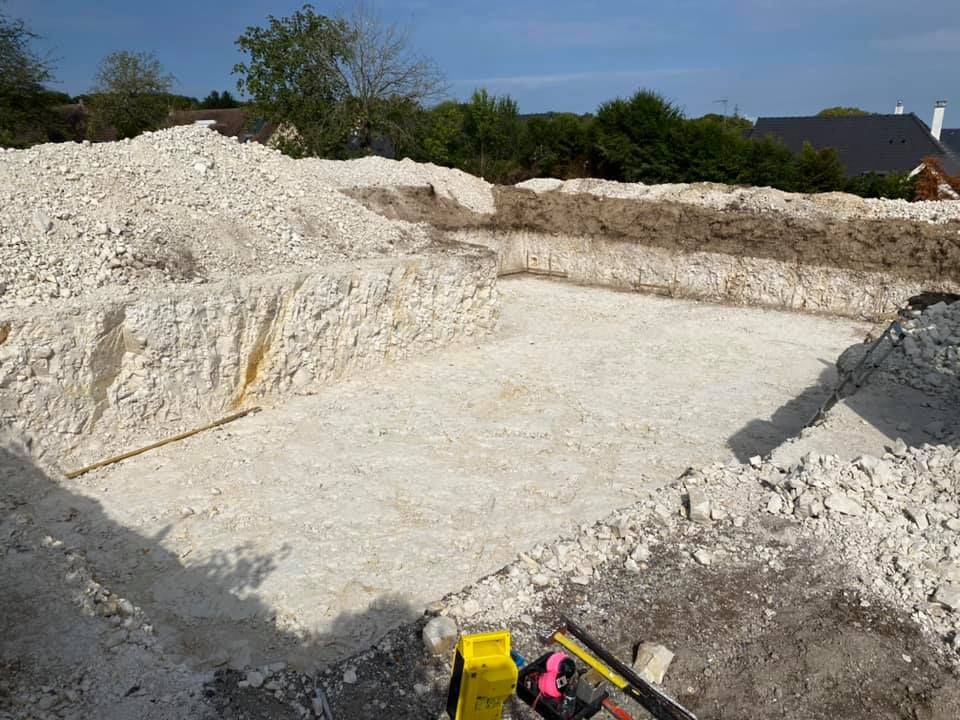 Grande gravière blanche aux parois excavées et au sol plat, avec des engins de chantier au premier plan.