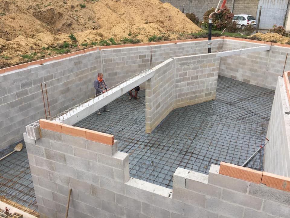 Fondations d'un bâtiment en blocs de béton en construction sur un terrain excavé, avec des ouvriers à l'intérieur et au-dessus.