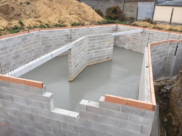 Piscine en blocs de béton en construction à flanc de colline, avec des eaux grises à l'intérieur et des murs inachevés.