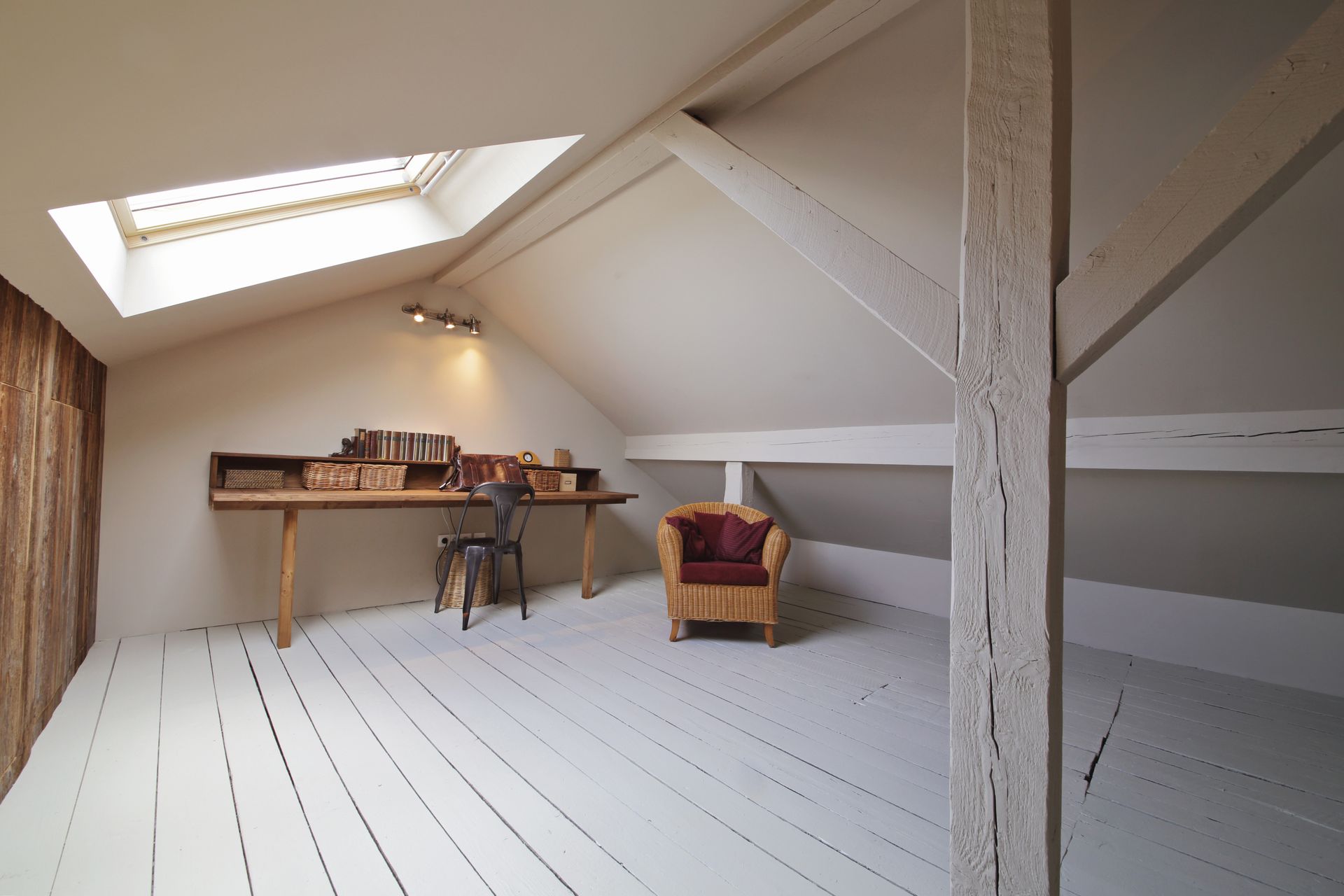 Espace de travail sous les combles avec puits de lumière, parquet blanc, bureau, chaise et fauteuil.