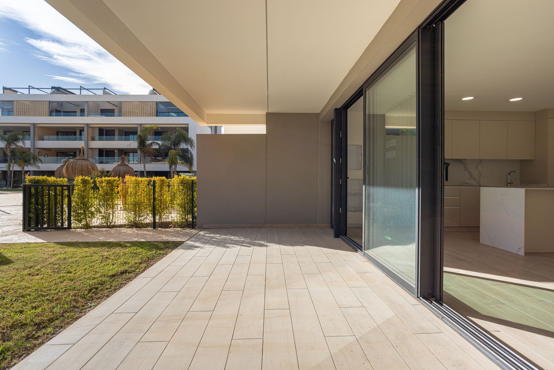 Patio d'appartement moderne avec sol carrelé, portes coulissantes en verre et vue sur les bâtiments voisins.
