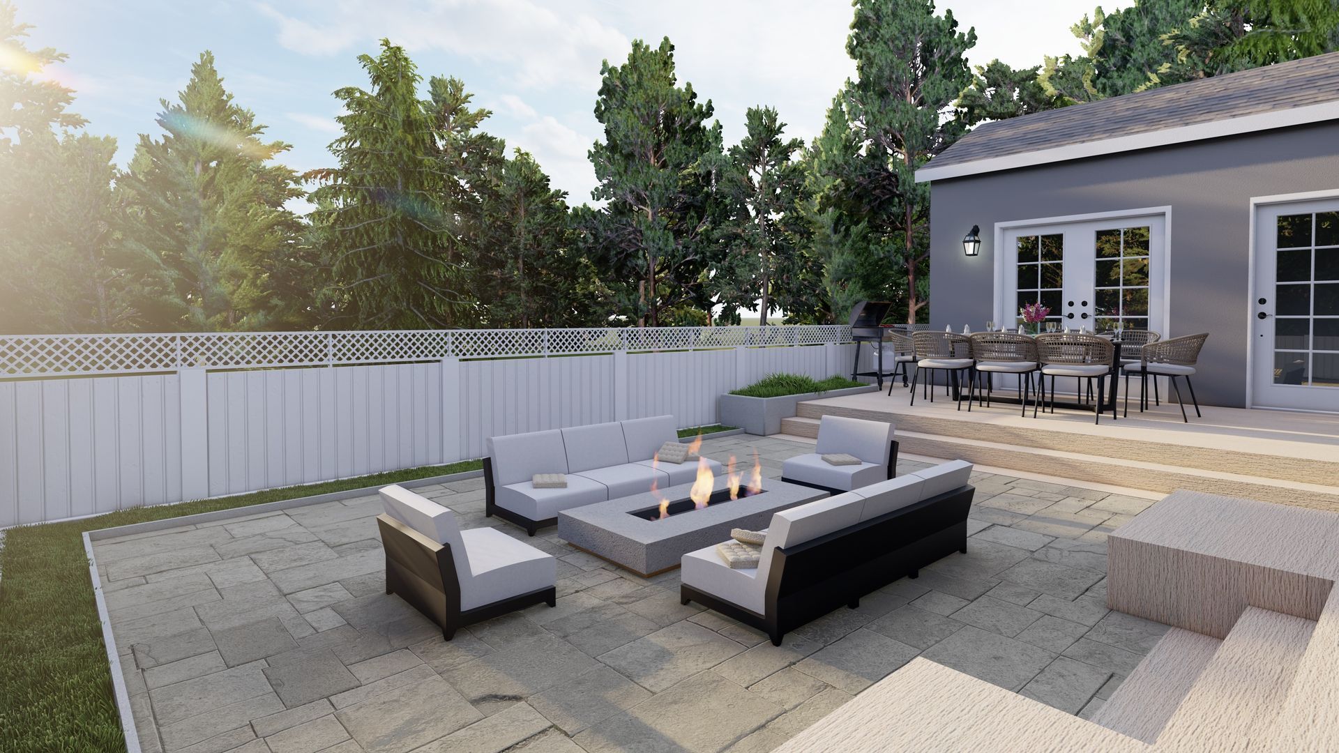 Terrasse avec canapé d'angle extérieur et foyer extérieur jouxtant une maison, bordée d'une clôture blanche et d'arbres.