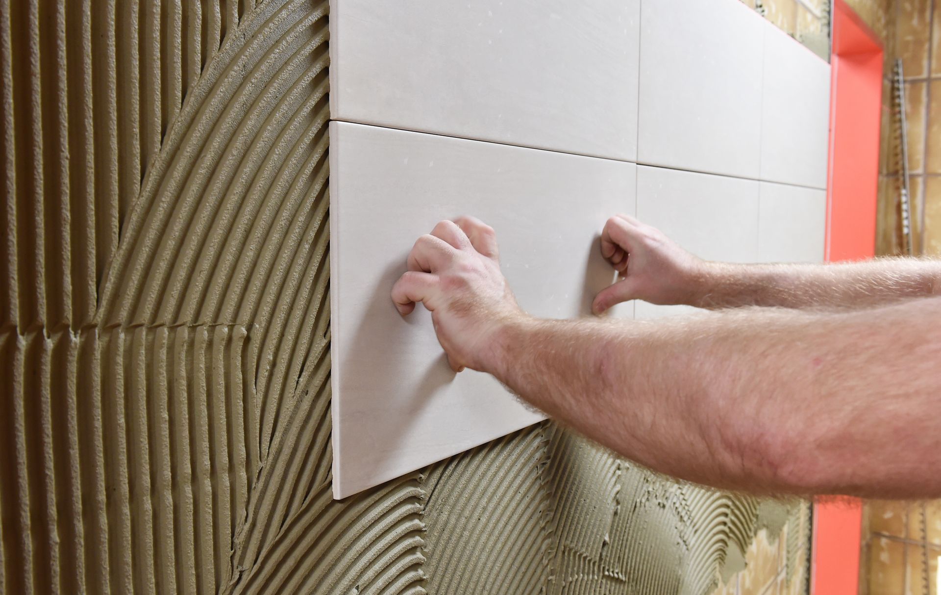 Des mains pressent des carreaux blancs sur un mur lors de travaux de construction ou de rénovation.