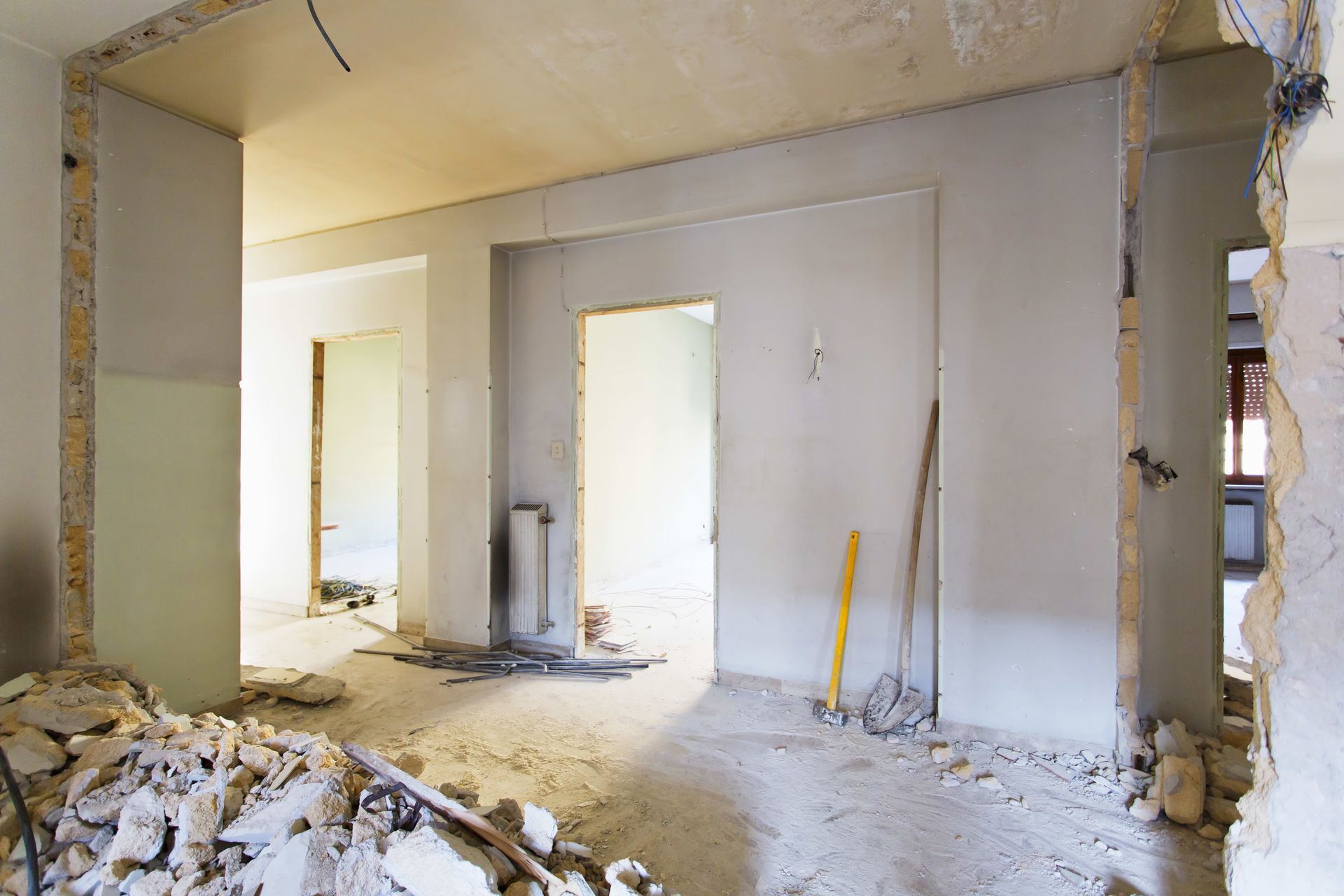 Pièce endommagée en cours de rénovation, avec des murs apparents, des débris et des outils appuyés contre un mur blanc.