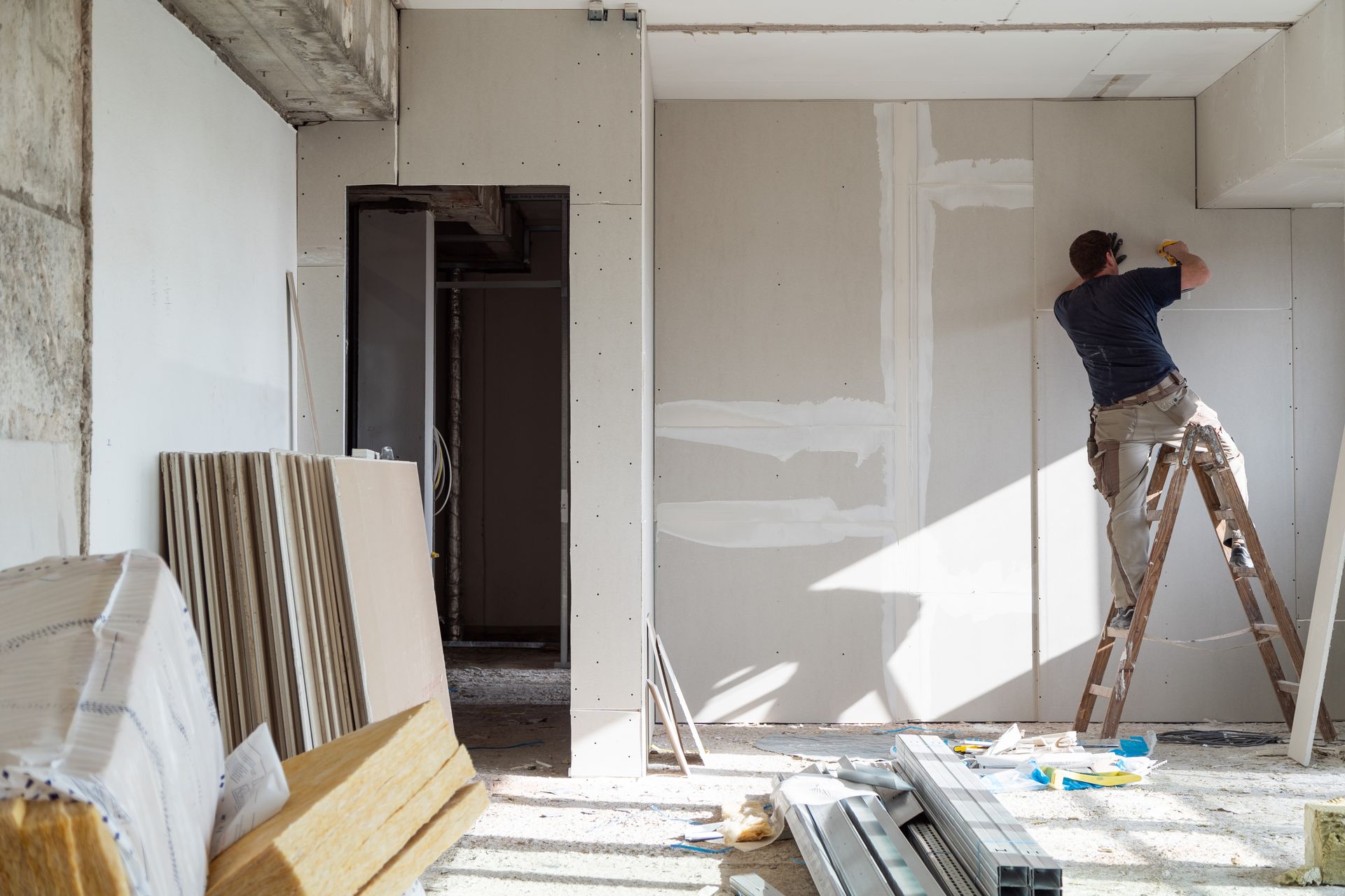 Un ouvrier enduit un mur dans une pièce inachevée, des matériaux de construction étant empilés à proximité.