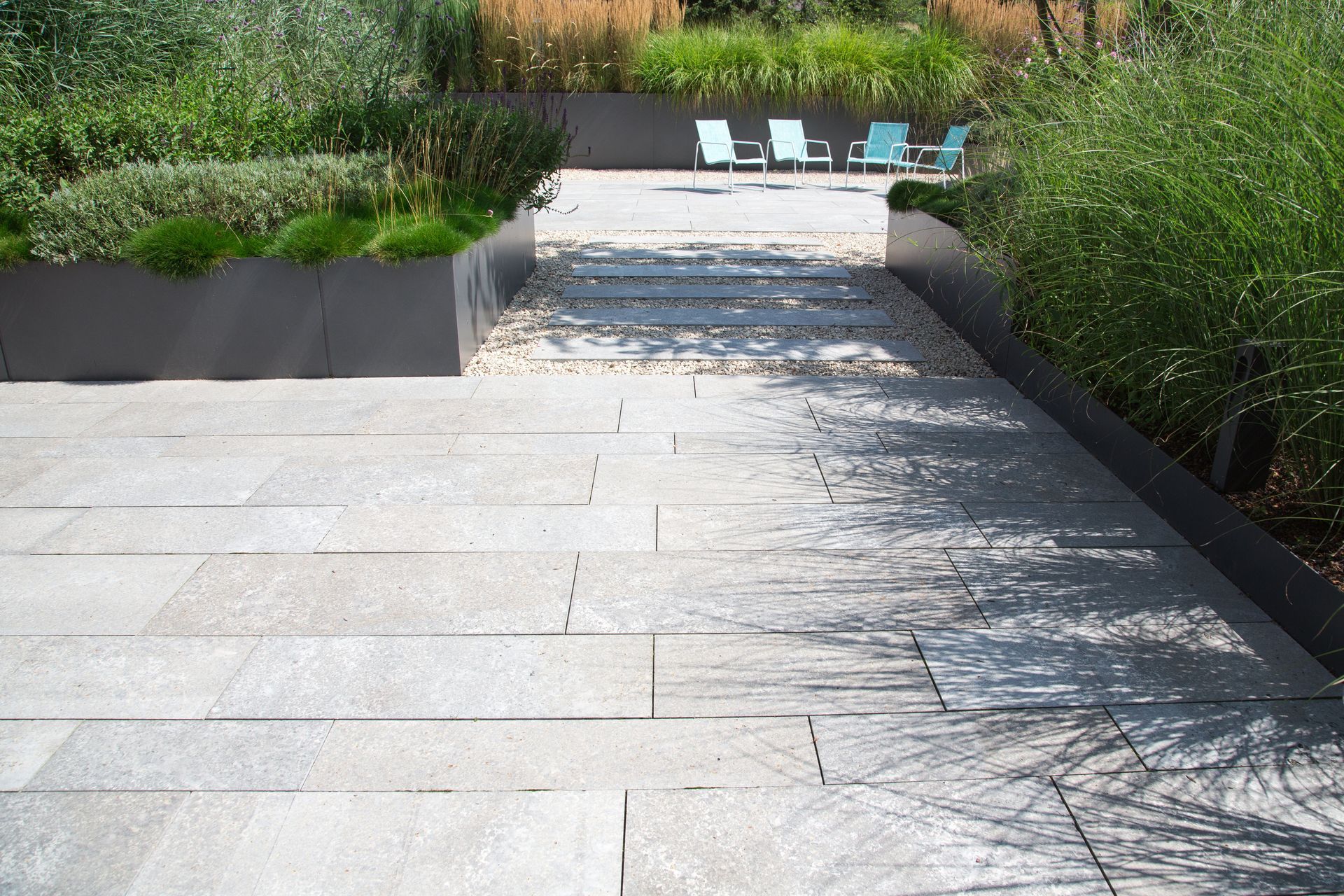 Des marches en pierre descendent vers un patio-jardin ensoleillé avec des chaises longues et de la verdure.