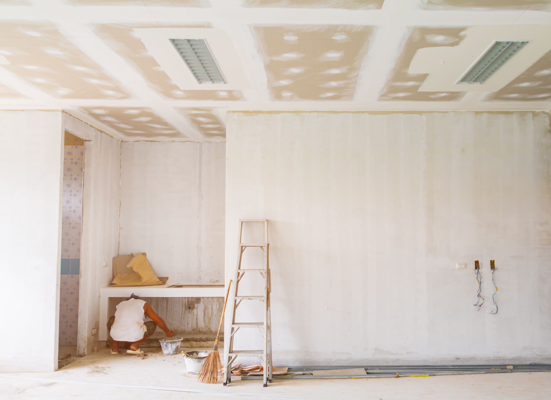 Pièce partiellement aménagée avec cloisons sèches blanches, plafond rebouché, échelle et outils de construction.