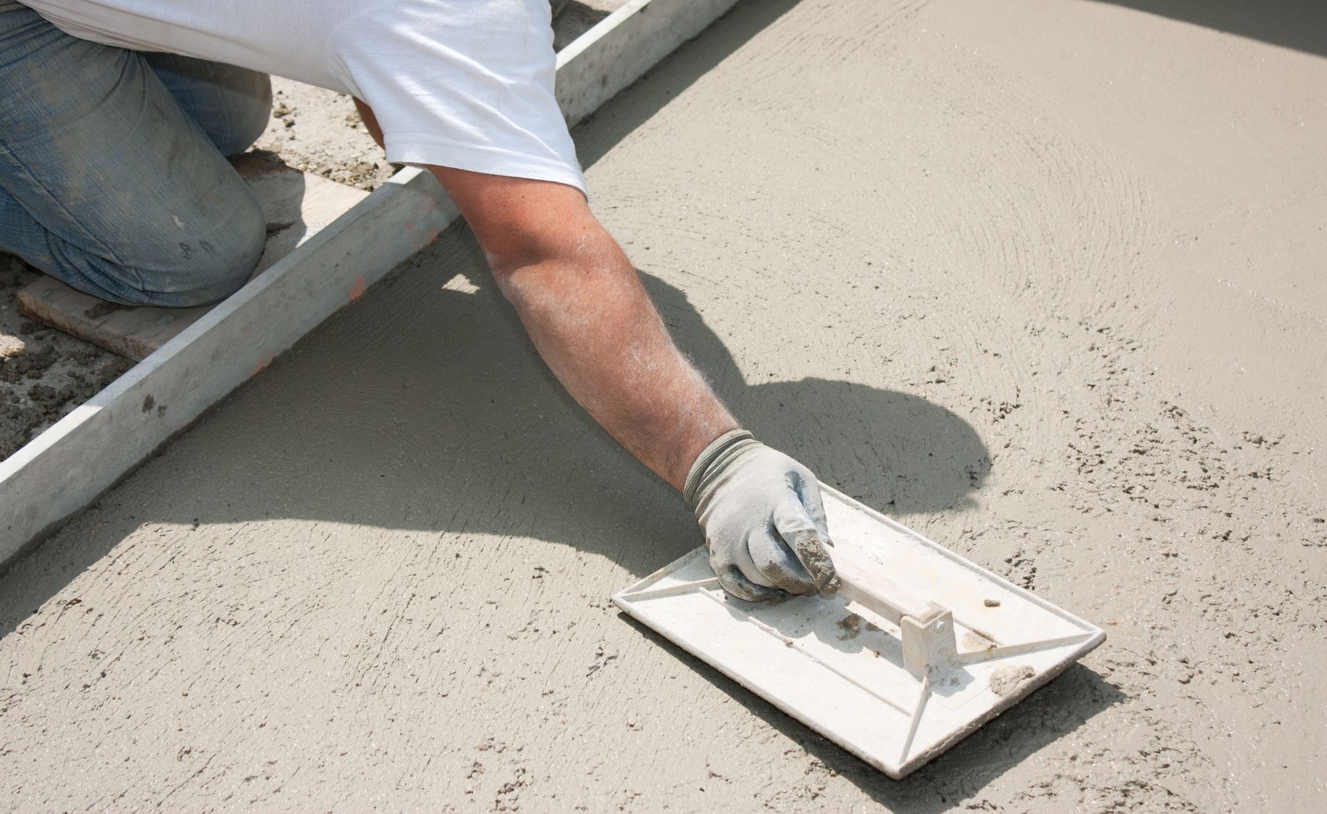 Ouvrier lissant du béton frais à la taloche sur une surface fraîchement coulée.