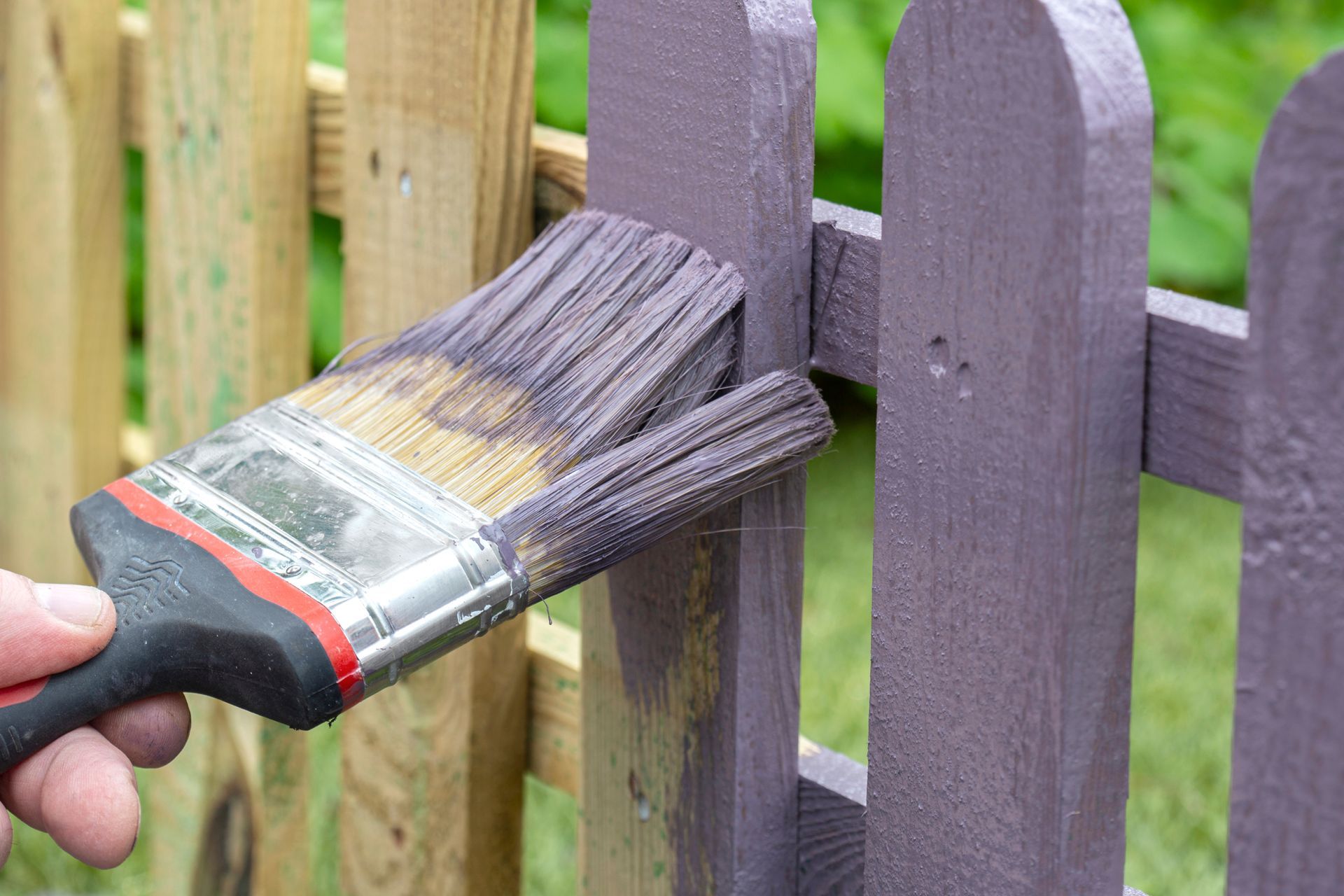 Un pinceau applique de la peinture violette sur un poteau de clôture en bois à l'extérieur.