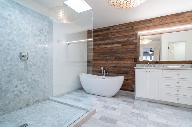 Salle de bains moderne avec douche en verre, baignoire en îlot, double vasque et mur d'accent en bois.