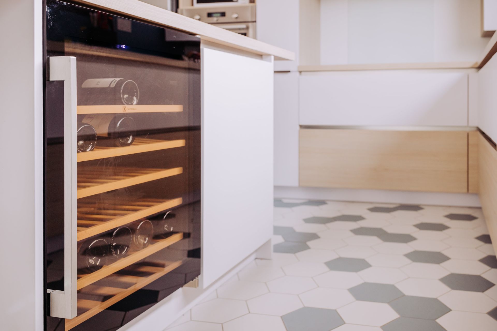 Cave à vin intégrée à côté de placards blancs dans une cuisine moderne avec sol carrelé en hexagones.