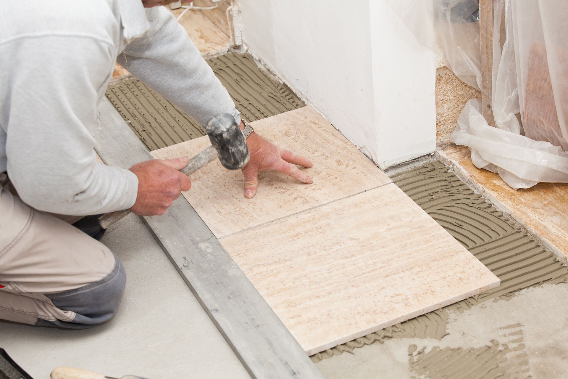 Un ouvrier pose un carrelage à l'aide d'une truelle et d'une règle métallique sur une surface en béton.