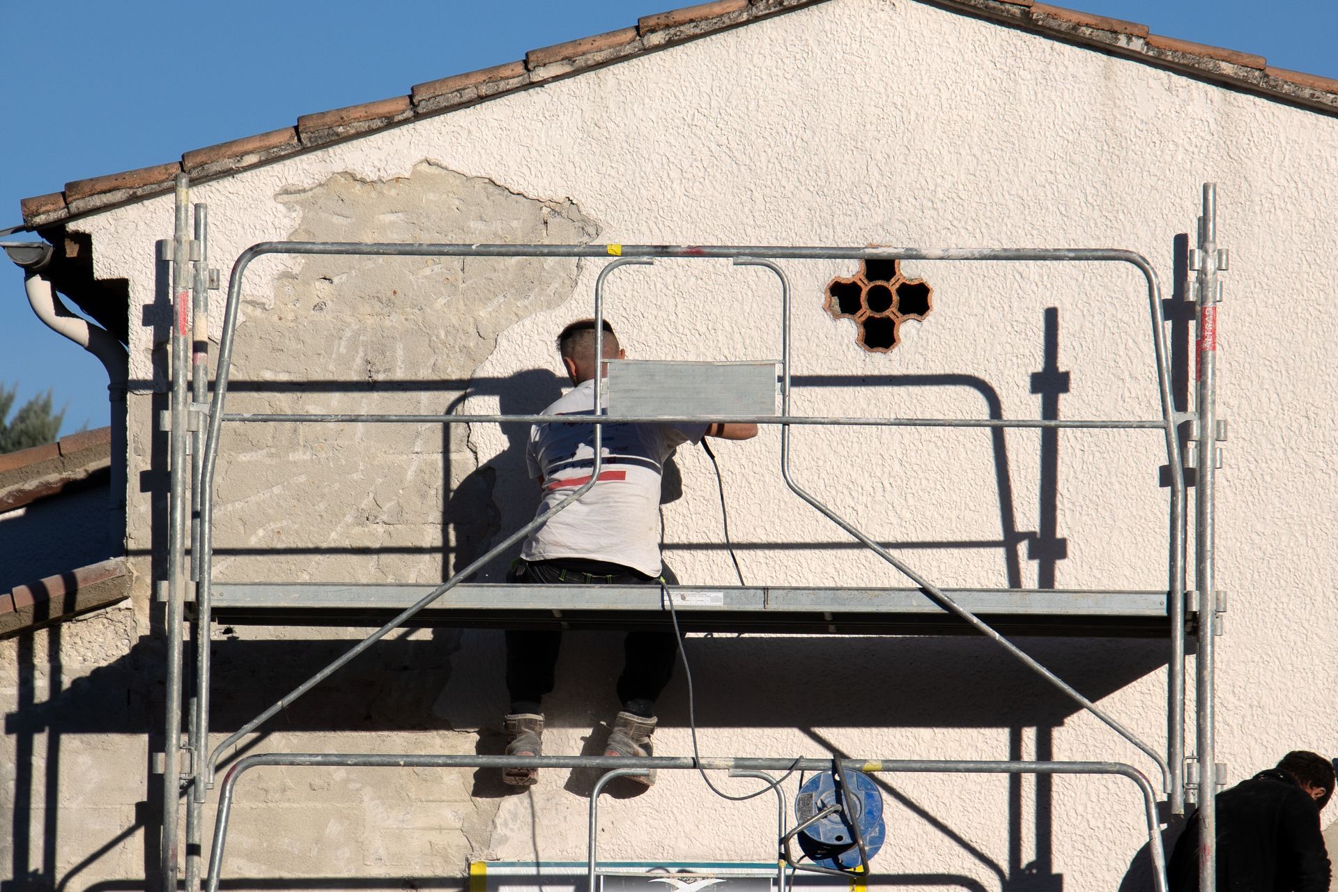 Ouvrier sur un échafaudage en train de peindre un mur en stuc sur l'extérieur d'un bâtiment.