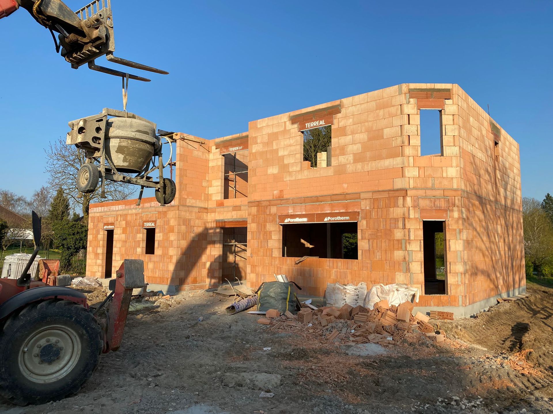 Maison en briques de deux étages en construction, avec une grue et des engins de chantier devant.