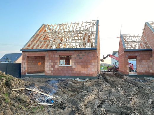 Maisons en briques partiellement construites avec charpente apparente sur un chantier boueux