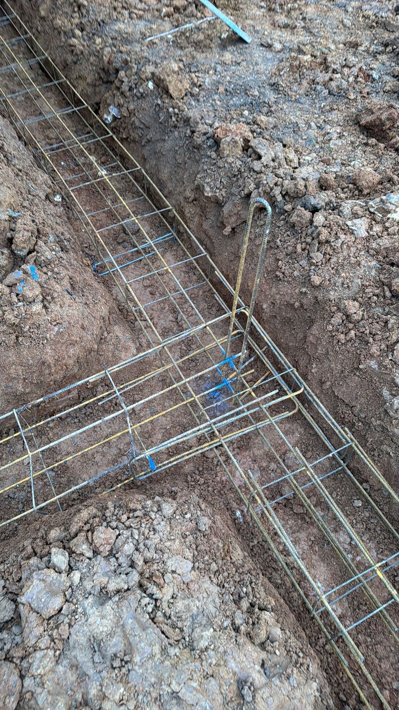 Treillis d'armatures posé dans une tranchée de terre, avec un petit lien bleu, en préparation de la fondation en béton.