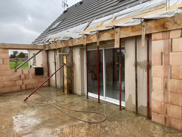 Maison partiellement construite avec des murs en briques inachevés, une charpente de toit et des portes coulissantes en verre en construction