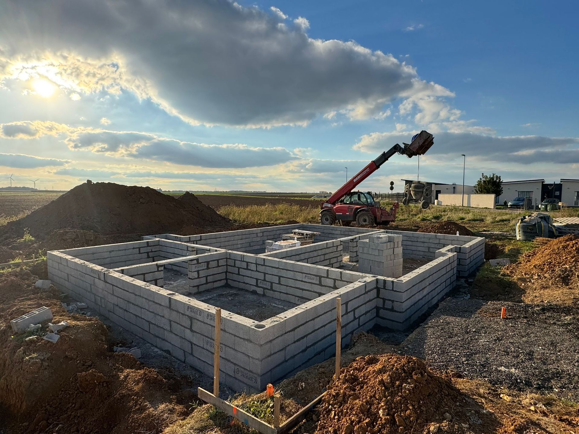 Blocs de fondation pour une maison en construction, avec une grue et des tas de terre au coucher du soleil.