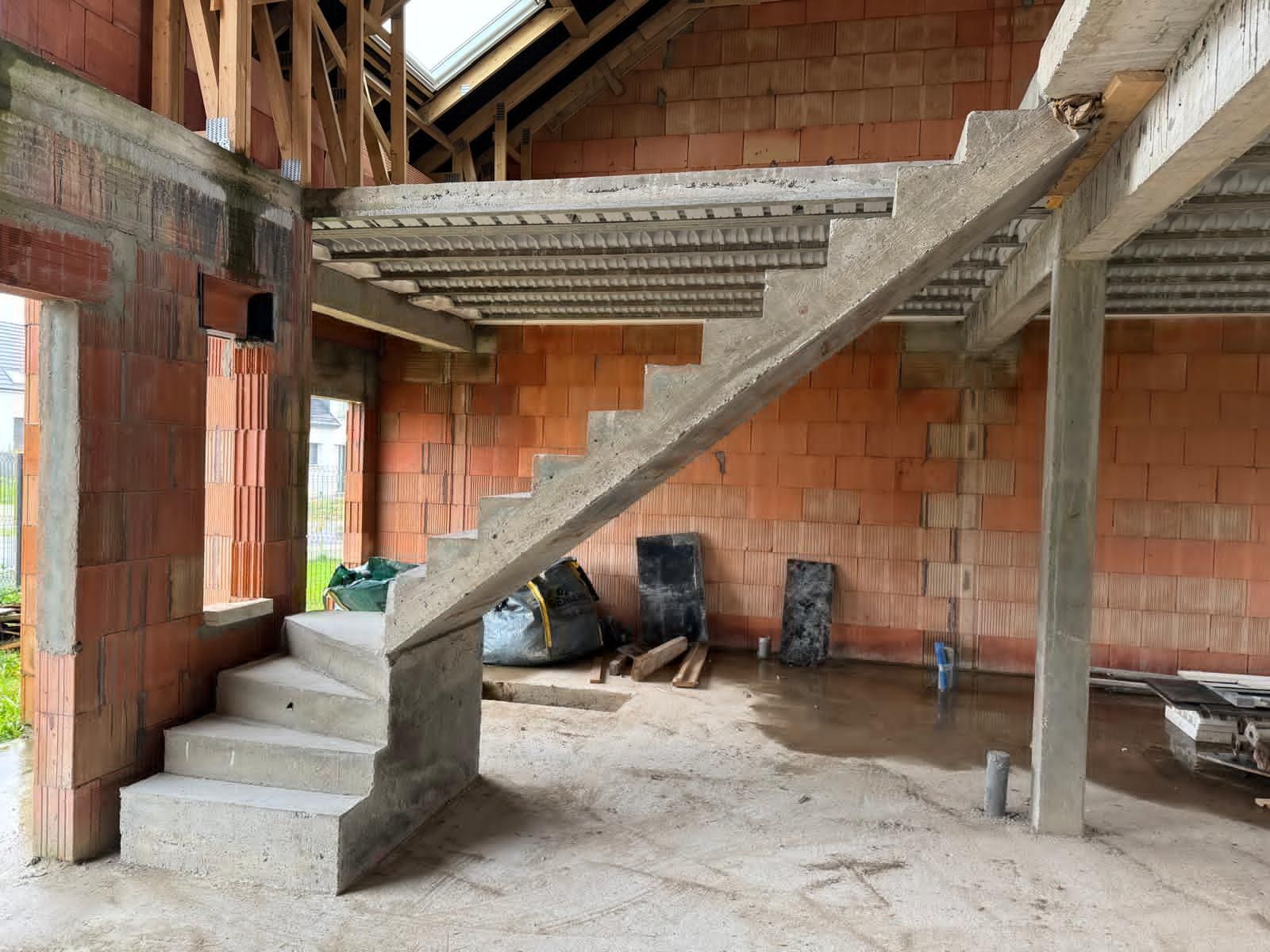 Intérieur en briques brutes avec escalier en béton, poutres apparentes et un animal noir se reposant près du mur du fond.