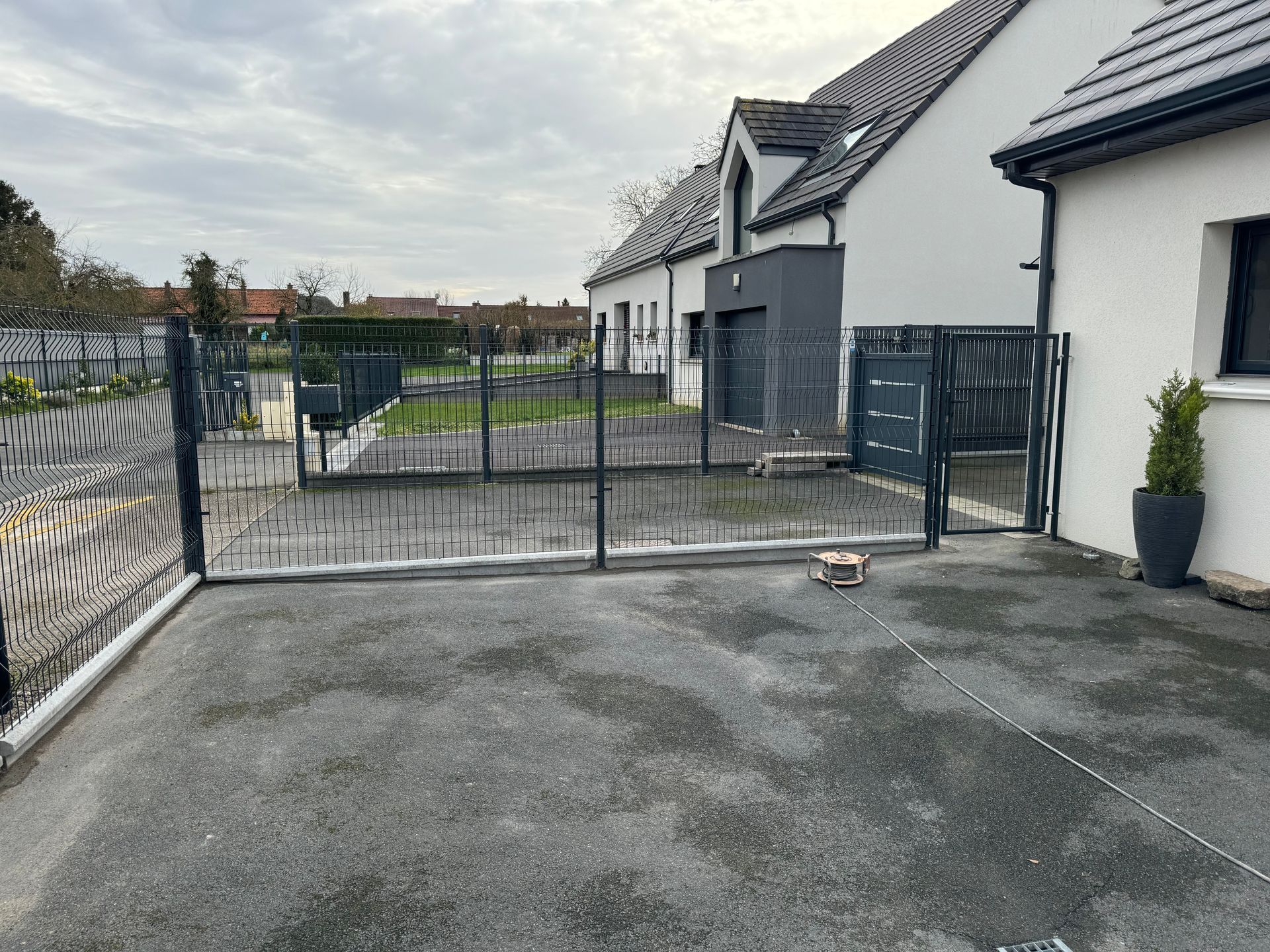 Allée privée fermée par un portail, longeant des maisons blanches aux pavés gris et une petite plante en pot.