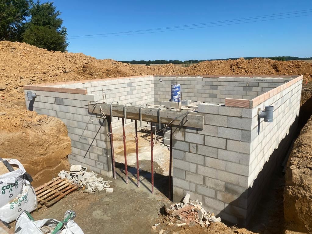 Sous-sol en parpaings partiellement construit sur un terrain vague, avec des barres d'armature et une bouteille d'eau bleue sur le dessus