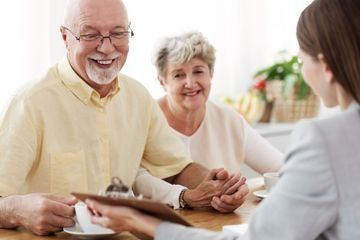 Una pareja de ancianos está sentada en una mesa hablando con una mujer.