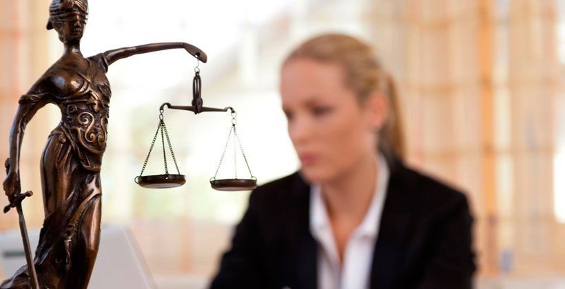 Una mujer está sentada frente a una estatua de la justicia sosteniendo una balanza de la justicia.