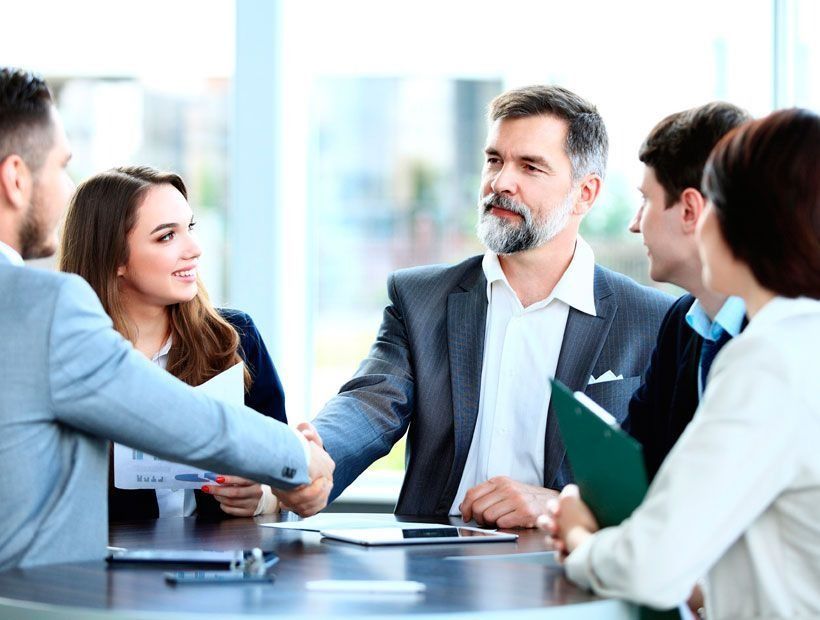 Un grupo de hombres de negocios están sentados alrededor de una mesa dándose la mano.