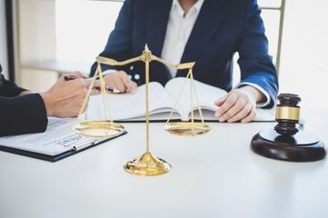 Un hombre y una mujer están sentados en una mesa con una balanza de justicia y un mazo.