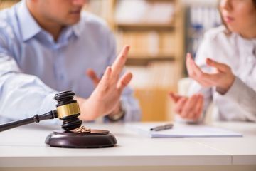 Un hombre y una mujer están sentados en una mesa con un mazo y un anillo de bodas sobre ella.