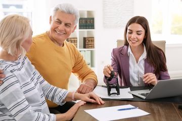 Una pareja de ancianos está sentada en una mesa con una mujer sosteniendo un sello.