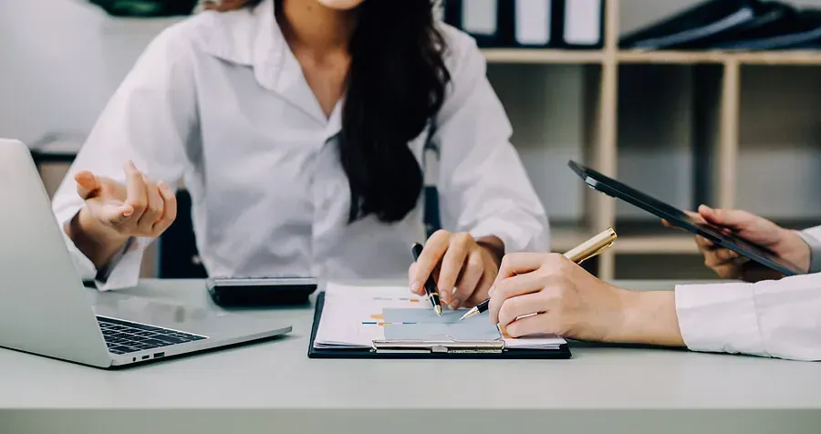 Una mujer está sentada en un escritorio con una computadora portátil y un portapapeles.