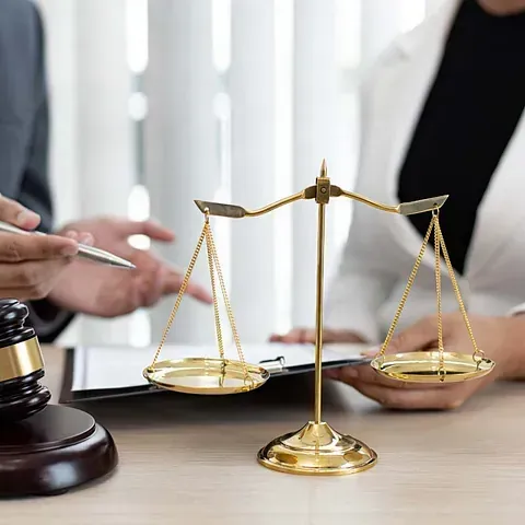 Un hombre y una mujer están sentados en una mesa con una balanza de justicia y un mazo.
