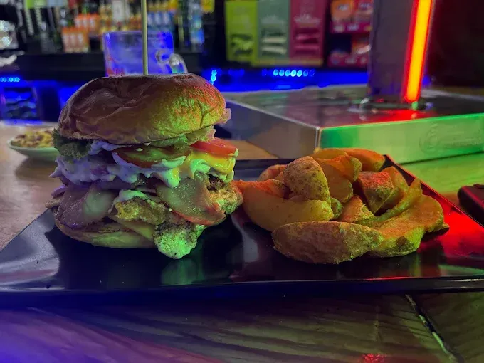 Hamburguesa con patatas fritas en plato negro, disposición tipo bar.