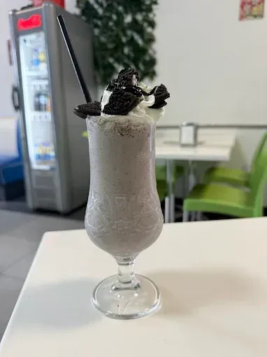 Batido de Oreo en vaso, con crema batida y galletas. Sobre una mesa blanca.