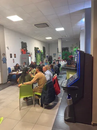 La gente se sienta a las mesas en un espacio interior bien iluminado. Se ve una máquina recreativa. 