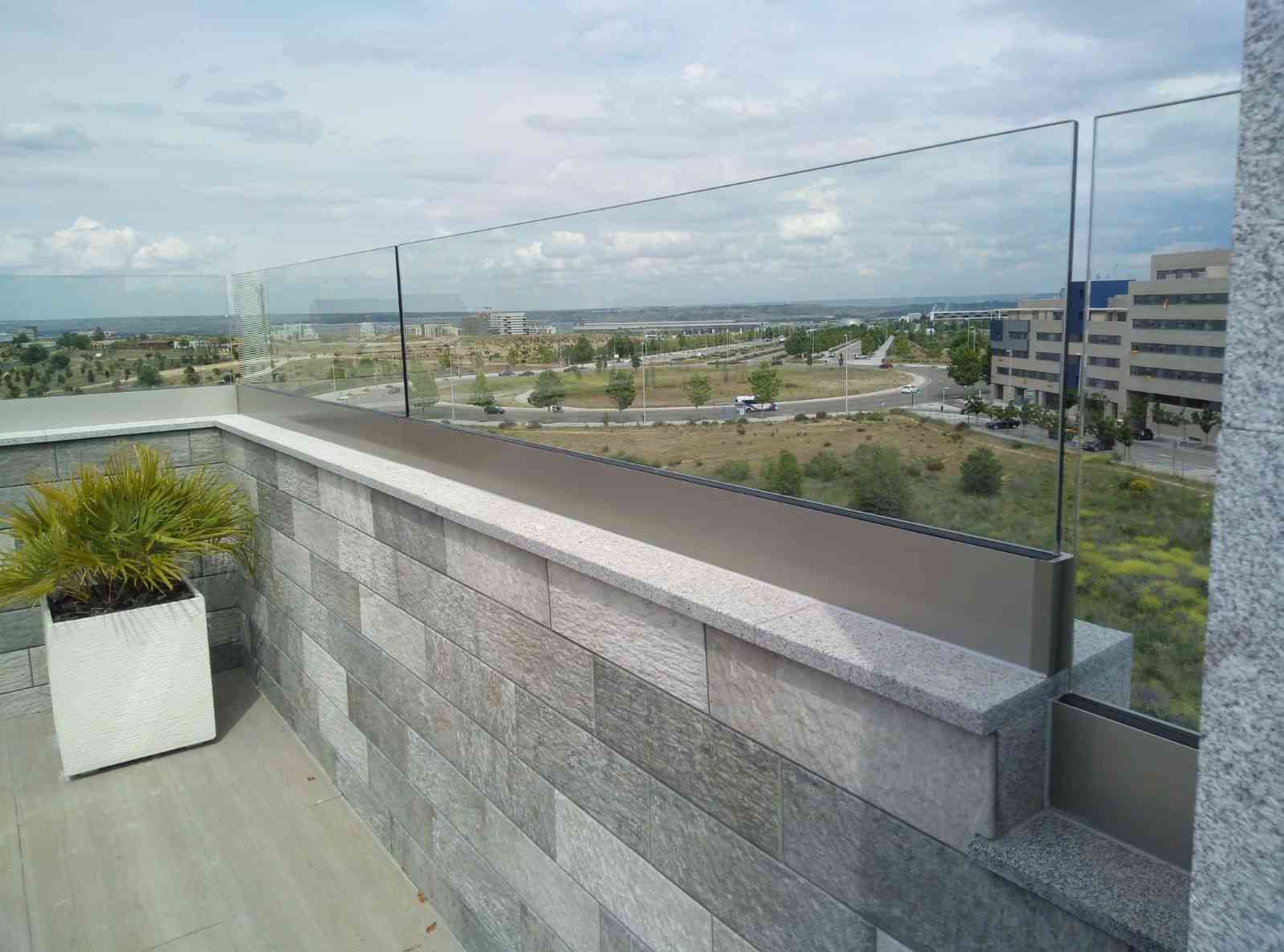 Terraza en la azotea con pared de piedra gris y barandilla de cristal con vistas a la ciudad y al paisaje.