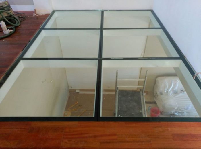 Suelo de cristal en un nivel inferior. Marco de rejilla negro con moldura de madera.