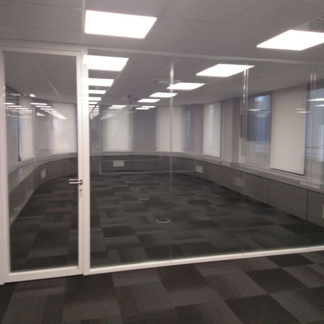 Una oficina moderna y vacía con paredes y puertas de vidrio, alfombra oscura y luces en el techo.