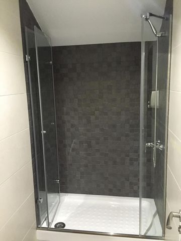 Una cabina de ducha moderna con puertas de vidrio, plato blanco y pared posterior de azulejos oscuros.