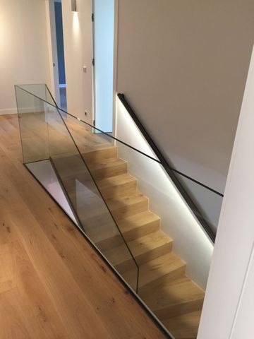 Escalera con barandilla de cristal, peldaños de madera y pasamanos negro con iluminación LED.