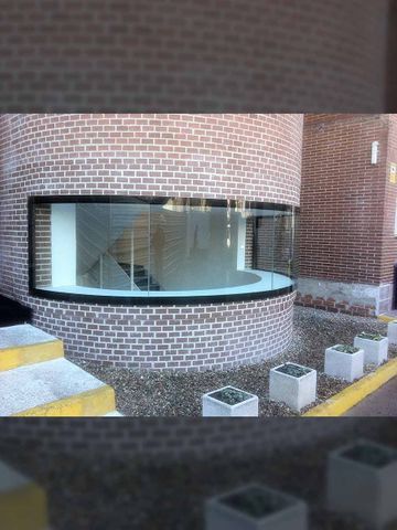 Edificio de ladrillo curvo con gran ventanal horizontal que revela una escalera; varias jardineras cuadradas en el frente.