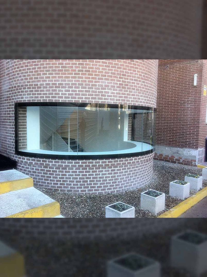 Edificio cilíndrico de ladrillo con ventana curva. Escalón y jardineras en la fachada.
