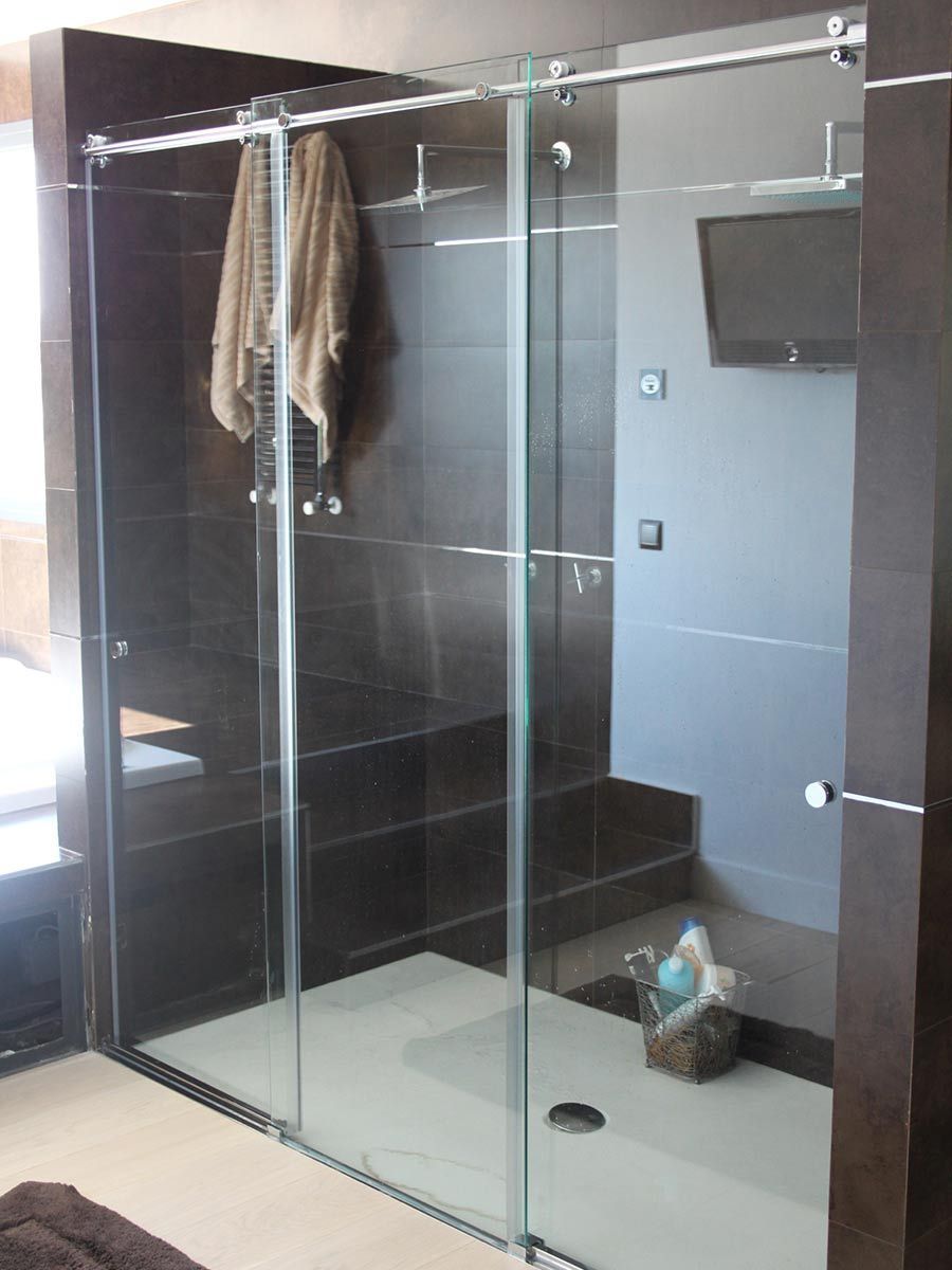 Cabina de ducha con puertas de cristal, azulejos beige, accesorios cromados.