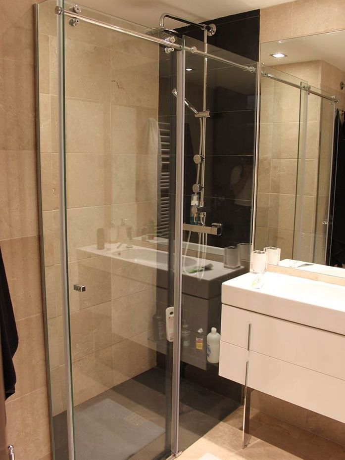 Mampara de ducha de cristal en un baño moderno. Tocador y espejo blancos.
