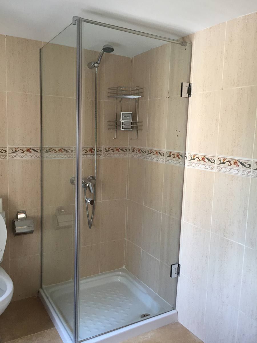 Cabina de ducha con puertas de cristal, azulejos beige, accesorios cromados.