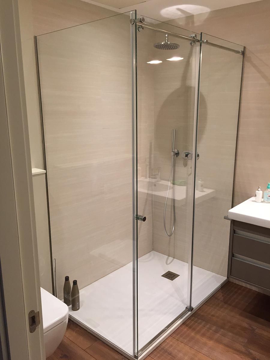 Mampara de ducha de cristal con pared de azulejos oscuros. Base de ducha blanca y paredes claras.