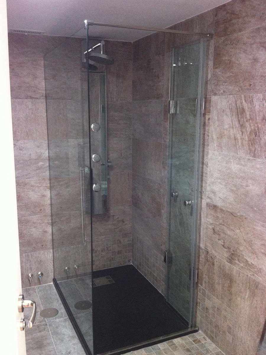 Ducha con paredes de vidrio, base oscura y accesorios plateados sobre paredes de azulejos marrones.