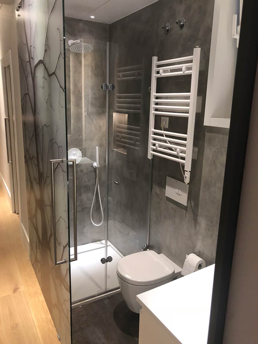 Ducha con paredes de vidrio, base oscura y accesorios plateados sobre paredes de azulejos marrones.