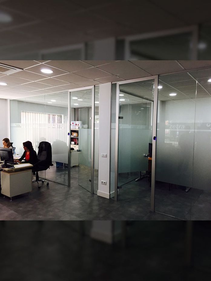 Espacio de oficina moderno con paredes de vidrio, empleados trabajando en escritorios y una oficina de vidrio esmerilado.